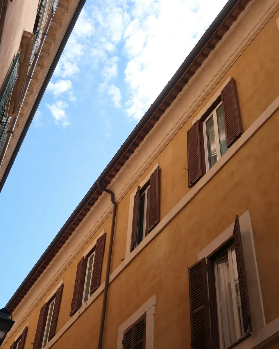 Facciata gialla di un palazzo di Roma con le persiane aperte
